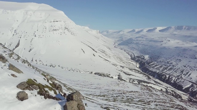 航拍，飞过冰雪覆盖的山脉，冰岛东部峡湾。冰岛乡村景观在春天或秋天的雪山季节之间。阳光明媚，适合旅游。视频素材