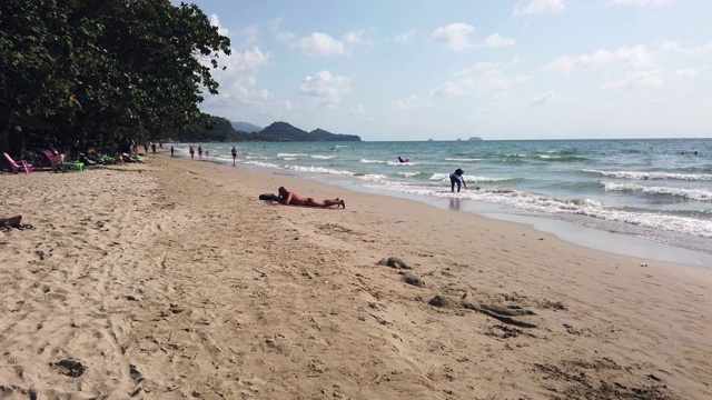 泰国Koh Chang - 2020年1月27日:在高昌岛的白色沙滩上，穿着泳衣的人们，穿着比基尼的妇女散步和日光浴的时间流逝。白云在蓝天上飞翔，棕榈树，夏天的时间视频素材