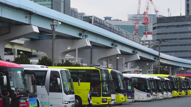 2018年1月19日，日本东京港区日出码头停车场，高架铁路“Yurikamome”(东京滨水新运输滨水线)在一排观光旅游巴士上方运行。视频素材