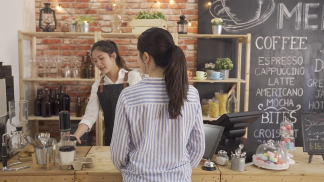 亚洲女酒保穿着围裙站在柜台，每天早上给常客一杯热茶，每天例行公事。办公室女职员在咖啡店用智能手机付款。服务员等待。视频素材