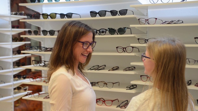漂亮的年轻女子选择新的眼镜与她的女儿在眼镜店视频素材