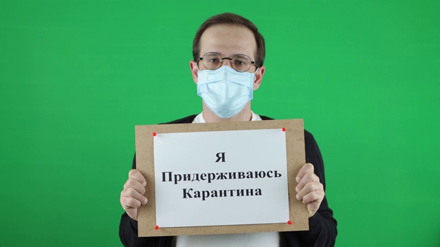 一个被隔离的年轻人欧洲的外观。戴着呼吸防护口罩绿色背景上刻着俄文"我坚持检疫视频素材