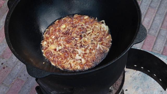 乌兹别克民族菜肴肉饭，肉饭，plov，米饭和肉放在大锅里。烹饪过程中，明火。在着火的釜中烹饪。准备阶段。把洋葱烤成焦糖色视频素材