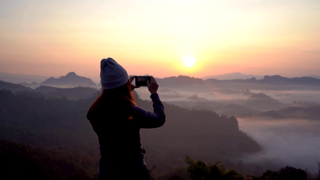 年轻女子旅行者与智能手机在雾海和日落的山在Mae Hong Son，泰国视频素材