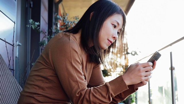 微笑的年轻女子在阳台上用智能手机的特写视频素材