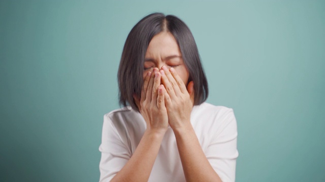 一名亚洲妇女发烧，打喷嚏，用纸巾擦鼻涕，站在孤立的蓝色背景。卫生保健的概念。4 k的视频。视频素材