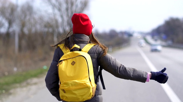 年轻漂亮的女人搭便车戴着红帽子，停下车。稳定拍摄，后视图视频素材