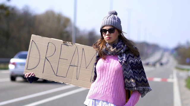 年轻漂亮的女人搭便车与海报梦想停车。视频素材