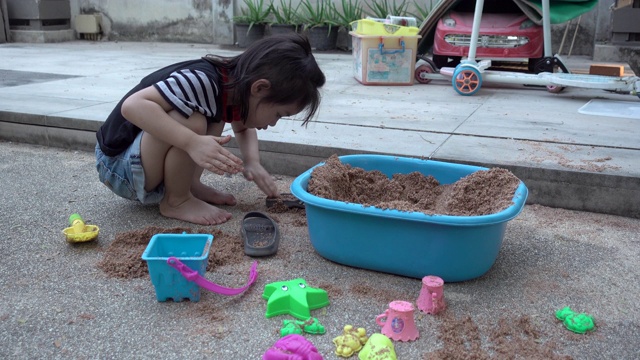 亚洲小女孩一起在院子里玩沙子玩得很开心。真实生活，手持拍摄视频素材