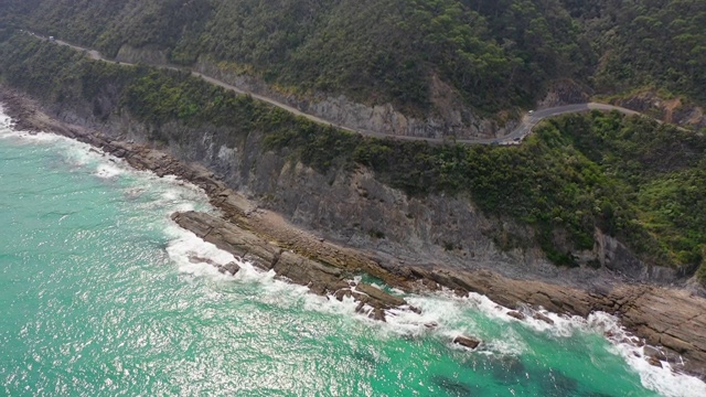 在阳光明媚的日子里，空中摇摄在悬崖上的道路上的车辆，无人机飞过海面，海浪溅在岩石上——Great Ocean road，澳大利亚视频素材