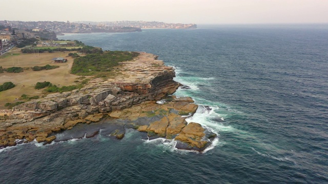 空中平移拍摄的海浪溅在岩石形成对天空，无人机飞越海洋城市-悉尼，澳大利亚视频素材