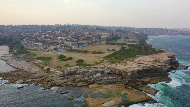 航拍海浪拍打岩石形成的城市，无人机飞向城市景观的天空-悉尼，澳大利亚视频素材