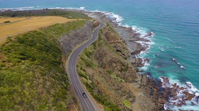 航拍的车辆上的道路上的岩石悬崖通过海上，无人机飞在海浪溅在海岸线上-大洋路，澳大利亚视频素材