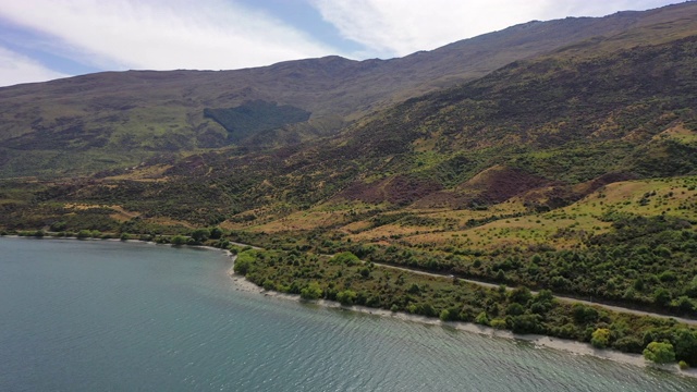 航拍的汽车在绿色植物的道路上的湖，无人机飞向山脉在阳光明媚的一天-皇后镇，新西兰视频素材