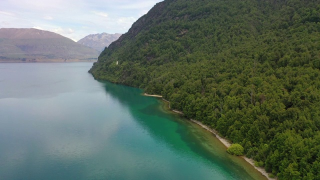 空中倾斜向下拍摄山上的绿树对天空，无人机飞过森林湖岸-皇后镇，新西兰视频素材