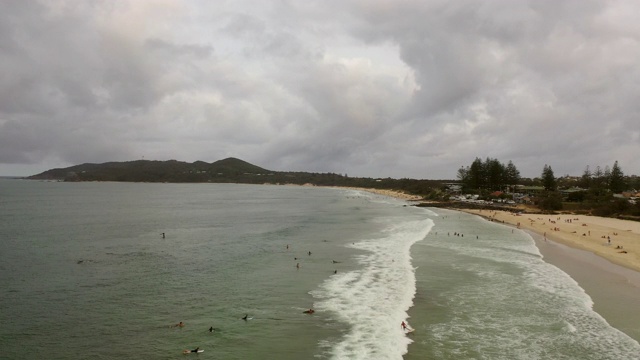 航拍海浪拍打海岸的人在海滩上，无人机飞行在多云的天空在阴天的海岸线上-拜伦湾，澳大利亚视频素材