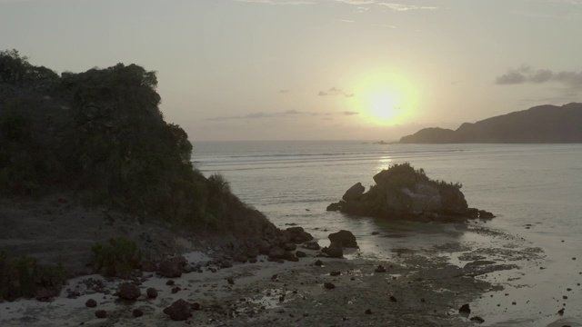 航拍的岩石形成在海上对天空日落，无人机向后飞行在海滩-龙目岛，印度尼西亚视频素材