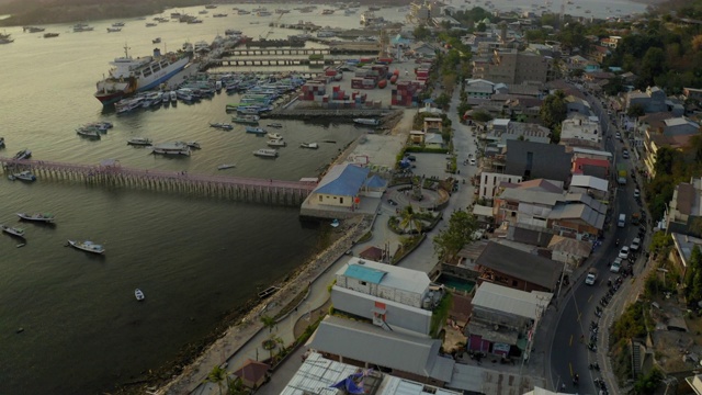 空中倾斜拍摄的沿海城市与天空的海港，无人机飞向海上的船只在日落-科莫多岛，印度尼西亚视频素材