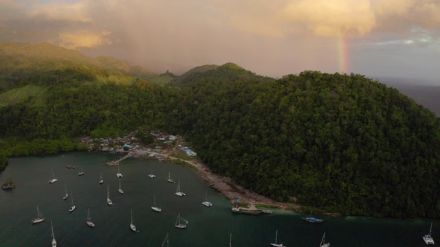 空中倾斜拍摄在彩虹附近的海面上的船只，无人机在村庄和山脉附近飞行——瓦卡托比摄政，印度尼西亚视频素材