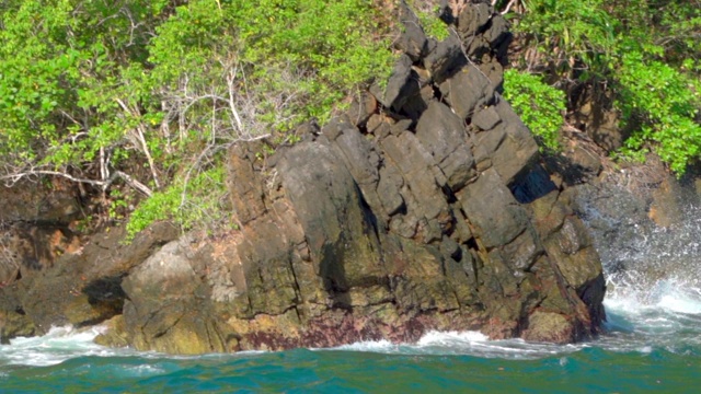 在阳光明媚的日子里，海浪拍打在海洋岩石上的绿色植物的慢动作拍摄-瓦卡托比摄制组，印度尼西亚视频素材