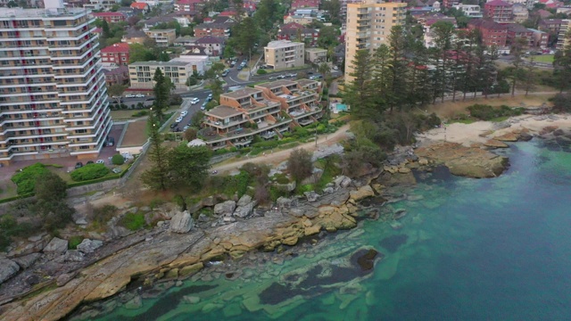 空中拍摄的岩石在建筑物和海洋中日落，无人机飞过停泊在城市-悉尼，澳大利亚视频素材