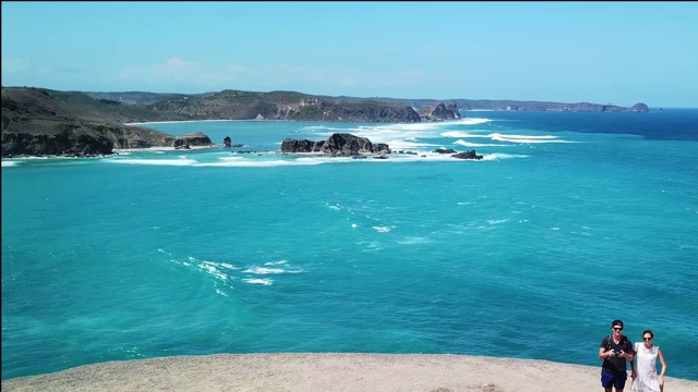 一架无人机拍摄到一对夫妇站在悬崖边欣赏风景。俯瞰印尼龙目岛丹戎安海滩。绿松石色的水。幸福和和睦视频素材