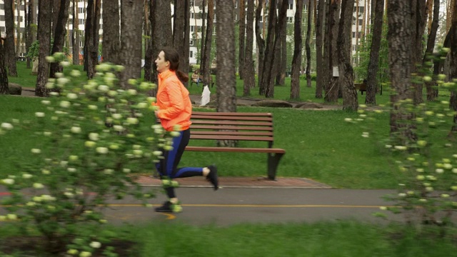 跑步的女人在雨中的城市公园里跑步，侧视图。运动健身女性在户外进行跑步锻炼。在公园小路上慢跑的运动员视频素材