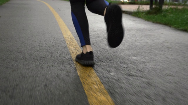 跑步女穿着运动鞋在城市公园慢跑。下雨天穿着运动鞋在公园小路上跑步的女运动员。健康的生活方式和运动理念视频素材