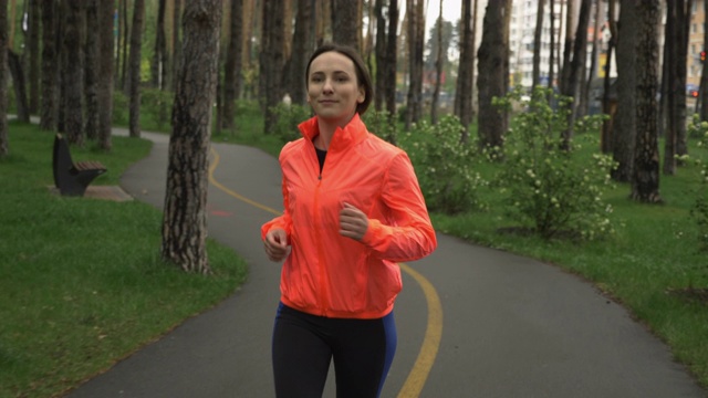 女跑步者在城市公园慢跑。下雨天独自在公园进行健身女性训练。运动运动员早上在林地的娱乐场所锻炼。健康的生活方式和跑步理念视频素材