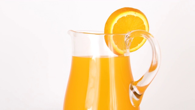 Close up of spinning jug with orange juice and slice of orange on white background特写旋转jug with orange juice and slice of orange on white background视频素材