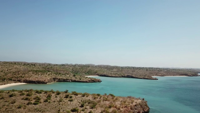 一架无人机在印度尼西亚龙目岛田园般的粉色海滩的海岸线上空飞行。海是平静的，闪烁着许多深浅不一的蓝色，温柔地冲刷着悬崖。大自然的美。未遭破坏的,隐藏的宝石视频素材