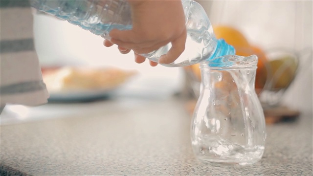 那男孩把塑料瓶里的水倒进一壶干净的饮用水里视频素材