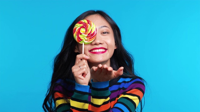 美丽的女人送飞吻和用彩色的棒棒糖遮住她的眼睛视频素材