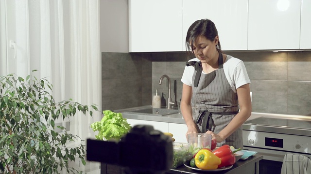 迷人的年轻女子在家里厨房用数码相机录制一段关于健康饮食的视频。视频博客和社交媒体概念。视频素材