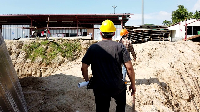 一名女性和一名男性建筑工人，建筑商，承包商，工程师沿着建筑工地前进。视频素材