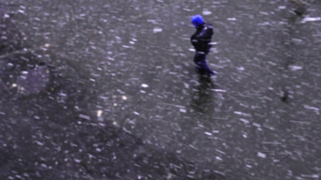 一个人走在飘落的雪下，上面的风景。冬天的街道视频素材