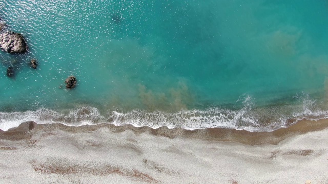 俯瞰碧绿的地中海海水在鹅卵石上翻滚。从空中俯瞰，透明的泡沫状海浪拍打着海岸上的石头。壮丽的泻湖在塞浦路斯度假胜地。相机移动。视频素材