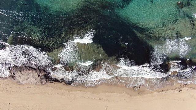 顶部鸟瞰图的沙海岸与泡沫透明波浪翻滚。镜头从塞浦路斯度假胜地地中海壮丽的泡沫水域向上移动。风光、山水、自然、美。视频素材