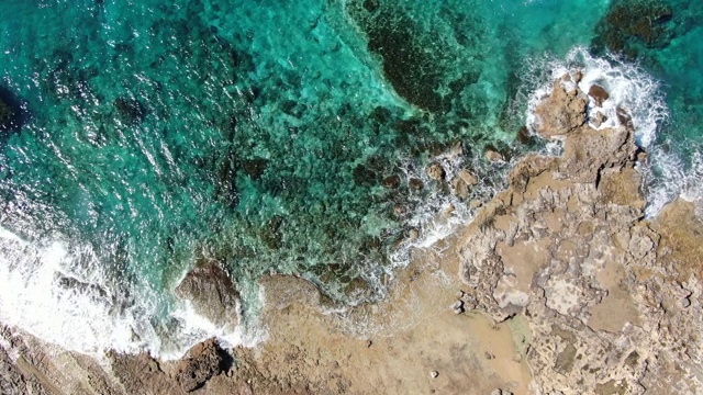 鸟瞰图的泡沫绿松石的海浪冲击在塞浦路斯度假胜地荒凉的岩石。镜头靠近透明的海水，在阳光下闪闪发光的海底石头。海景,自然,旅游。视频素材