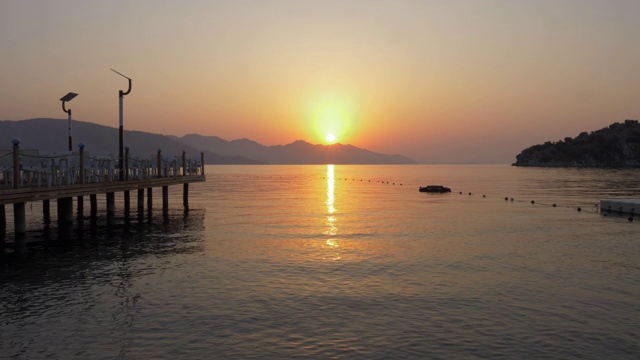 时光流逝的日出风景，山海景观。清晨的太阳升起在山的轮廓和平静的海水。金色的黎明在海滩码头的背景。视频素材