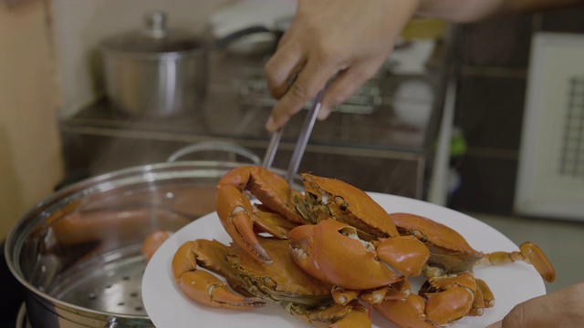 厨房里用钳子从锅里夹起煮熟的蓝蟹的女人视频素材