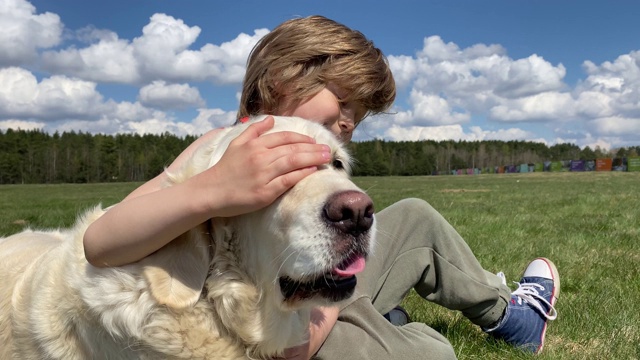 对宠物的爱。美丽的金毛猎犬带着一个小男孩在阳光明媚的夏日的田野里休息，慢镜头视频素材