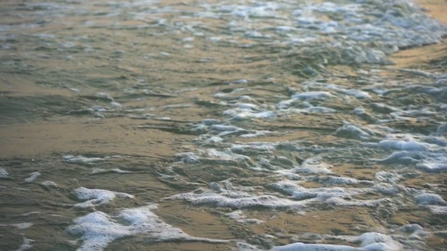 特写海浪的缓慢运动，吹向海岸在晚上。夏天的海滩与金黄的波浪泡沫在日落时间和黄昏的天空。视频素材