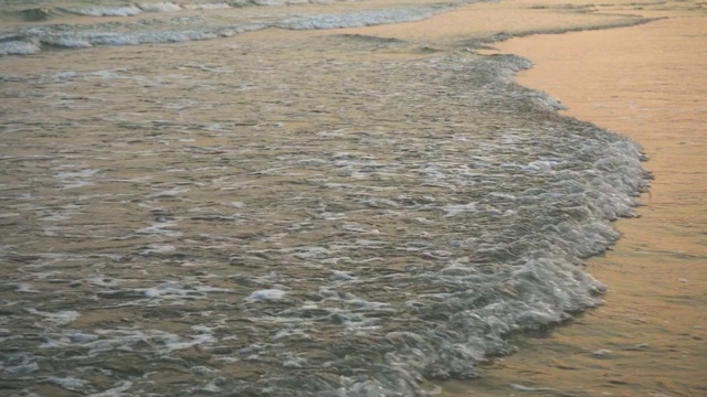 特写海浪的缓慢运动，吹向海岸在晚上。夏天的海滩与金黄的波浪泡沫在日落时间和黄昏的天空。视频下载