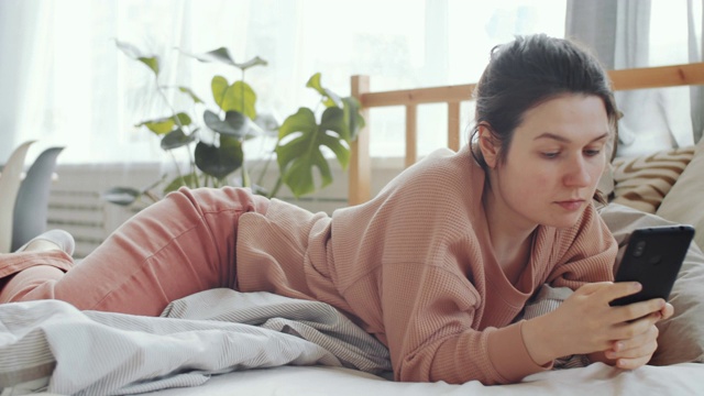 年轻女子躺在家里的床上使用手机视频素材