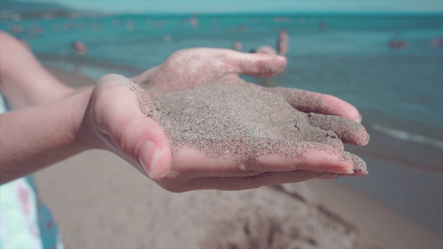 把沙子倒在女人的手里。夏天在海滩。阳光明媚的午后，细沙从指缝间滑落，美丽迷人的少女。视频素材