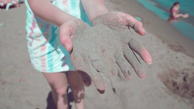 把沙子倒在女人的手里。夏天在海滩。阳光明媚的午后，细沙从指缝间滑落，美丽迷人的少女。视频素材