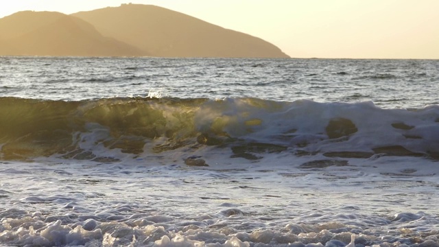 慢动作的海浪在黎明的背景下，海岸的山丘波光在太阳视频素材
