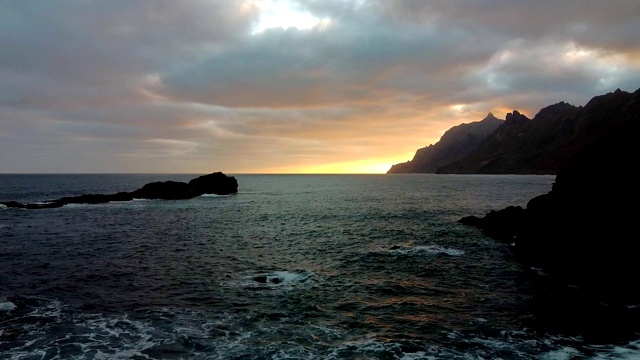 早晨日出黄昏。海浪拍打着海岸。无人机拍摄的4k画面，海浪拍打着岩石。太阳从山后的地平线升起。慢动作视频素材