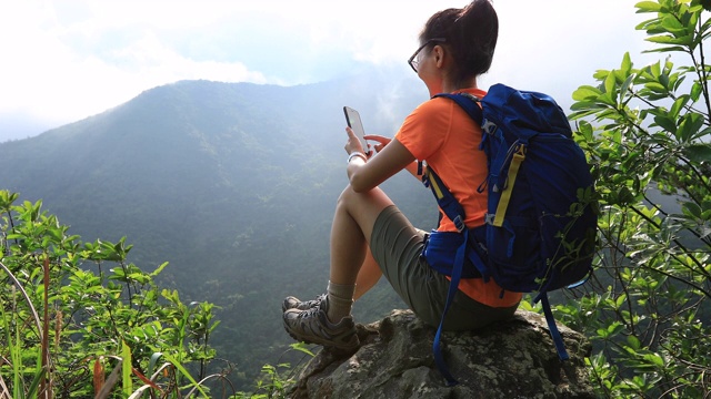 成功的徒步旅行者使用智能手机在日出的山顶悬崖边缘视频素材